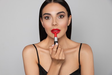 Young woman applying red lipstick on light gray background