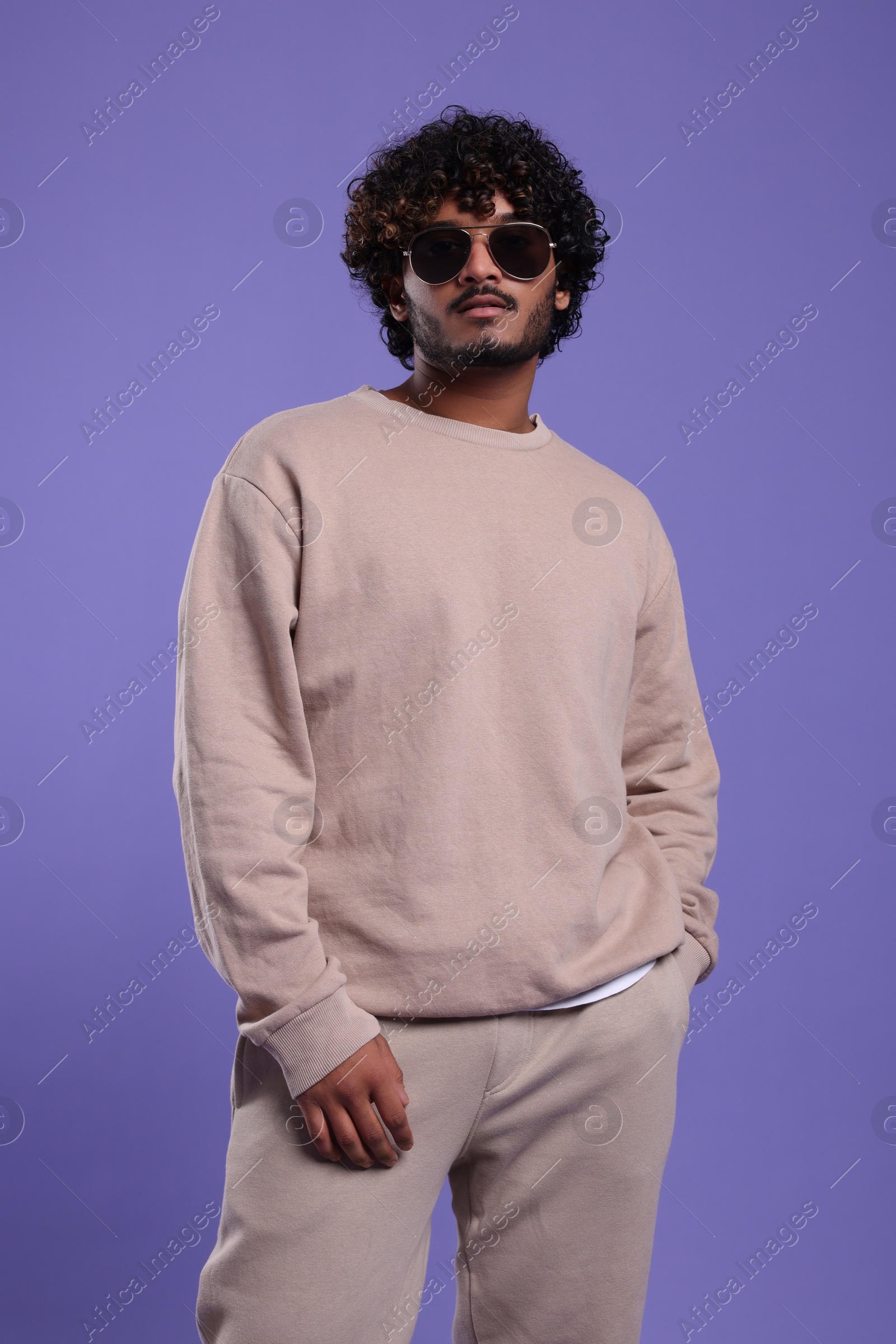 Photo of Handsome young man in sunglasses on violet background