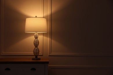 Photo of Stylish glowing night lamp on table in room. Space for text