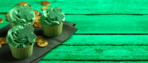 Image of St. Patrick's day. Tasty cupcakes with clover leaf toppers and cream on green wooden table, closeup. Banner design with space for text