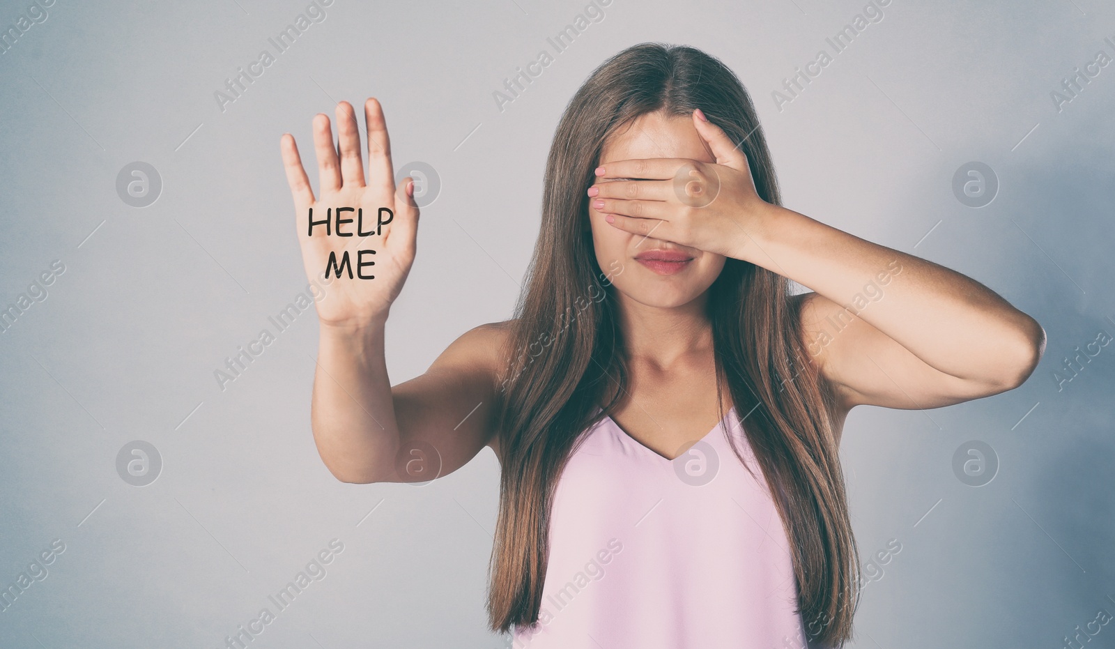 Image of Young woman with text HELP ME on her hand near grey wall