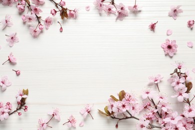 Photo of Frame of beautiful spring tree blossoms on white wooden table, flat lay. Space for text