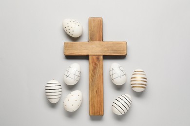 Wooden cross and painted Easter eggs on light grey background, flat lay