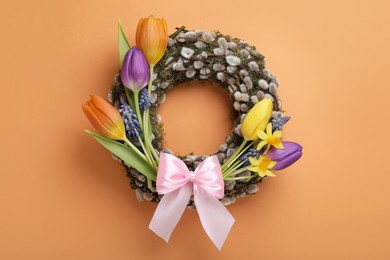 Willow wreath with different beautiful flowers and pink bow on orange background, top view