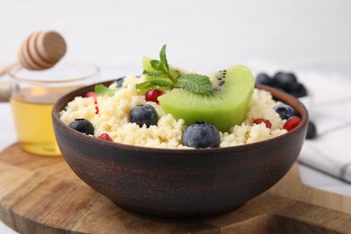 Photo of Bowl of tasty couscous with kiwi, blueberries and pomegranate on table, closeup