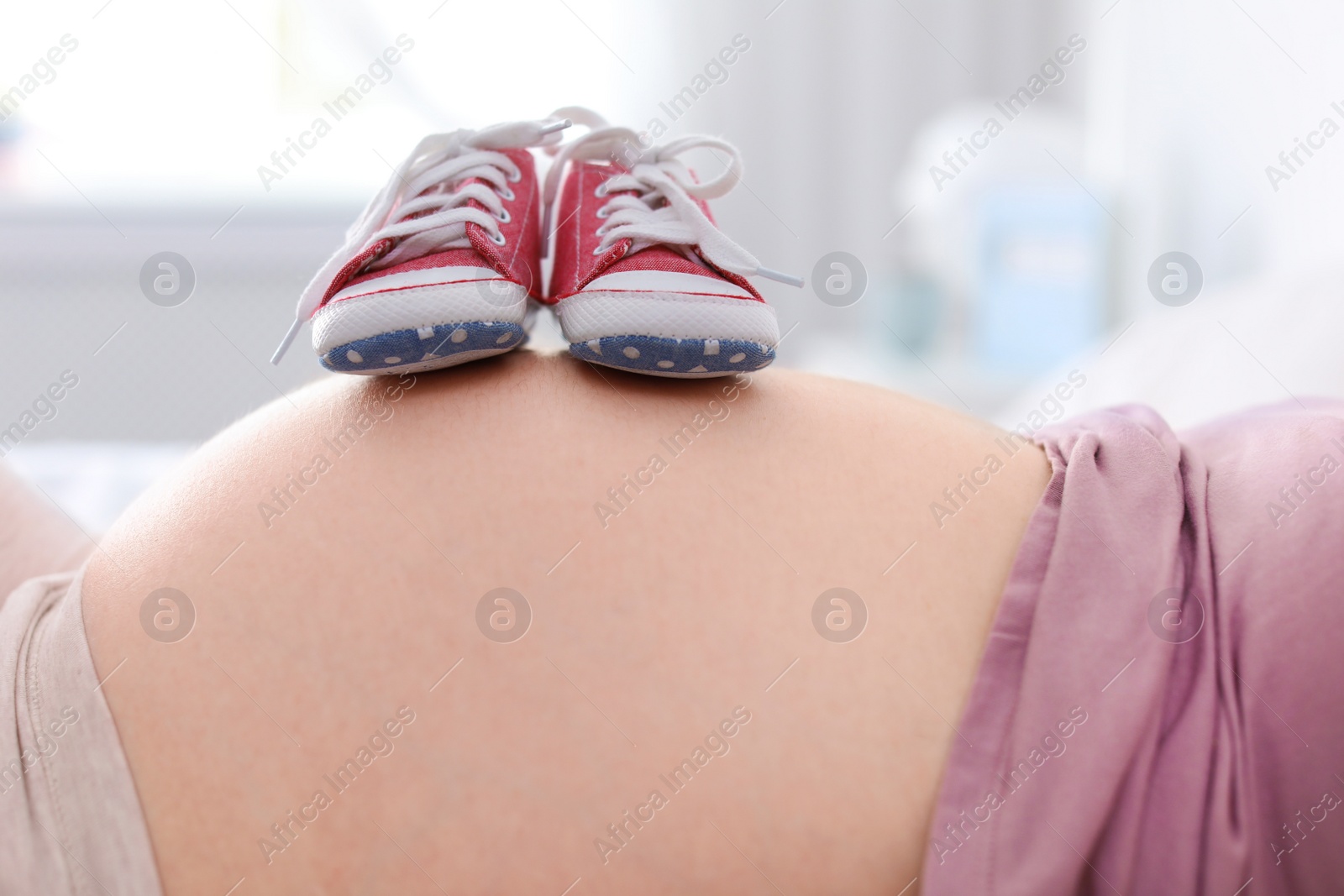 Photo of Pregnant woman with baby booties on blurred background, closeup view