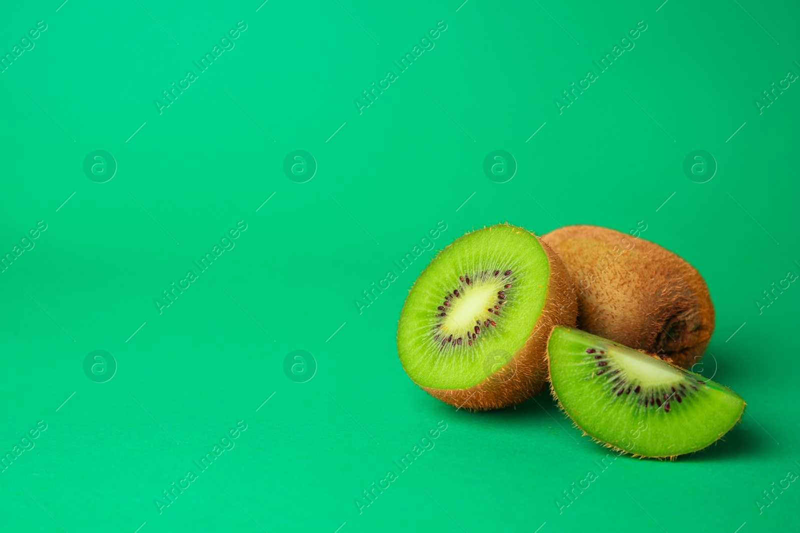 Photo of Whole and cut fresh kiwis on green background, space for text