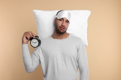Photo of Tired man with sleep mask and alarm clock on beige background. Insomnia problem