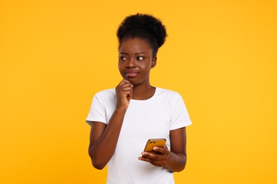 Beautiful young woman with smartphone on orange background