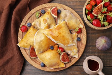 Delicious samosas with figs and berries on wooden table, flat lay