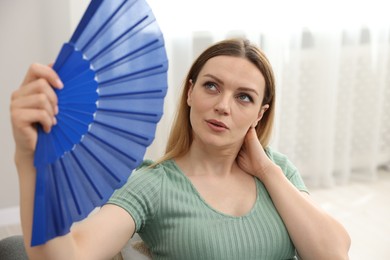 Woman waving blue hand fan to cool herself on sofa at home