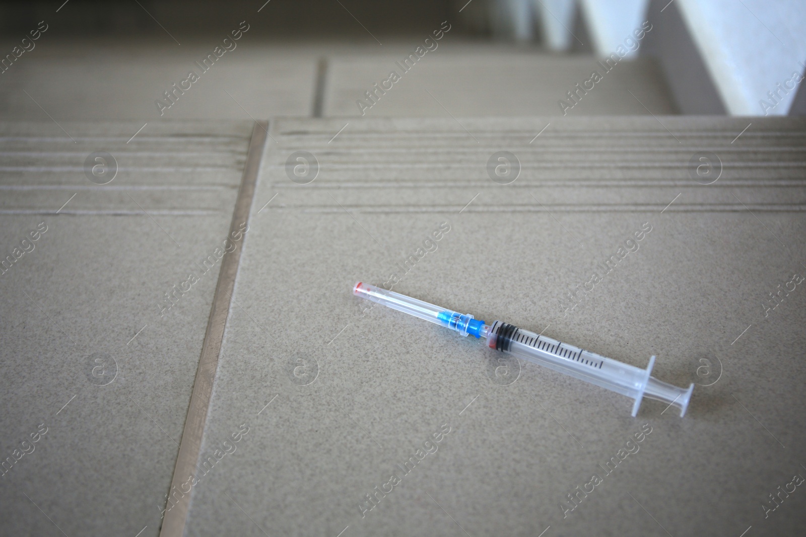 Photo of Disposable syringe with needle on tiled stairs indoors. Space for text