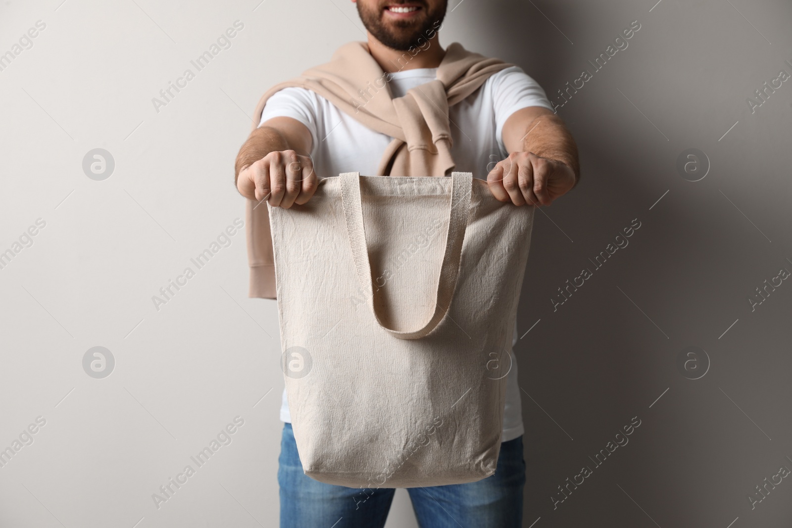 Photo of Happy young man with eco bag on light background, closeup