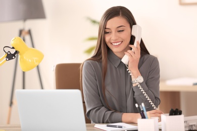 Photo of Young woman talking on phone at workplace