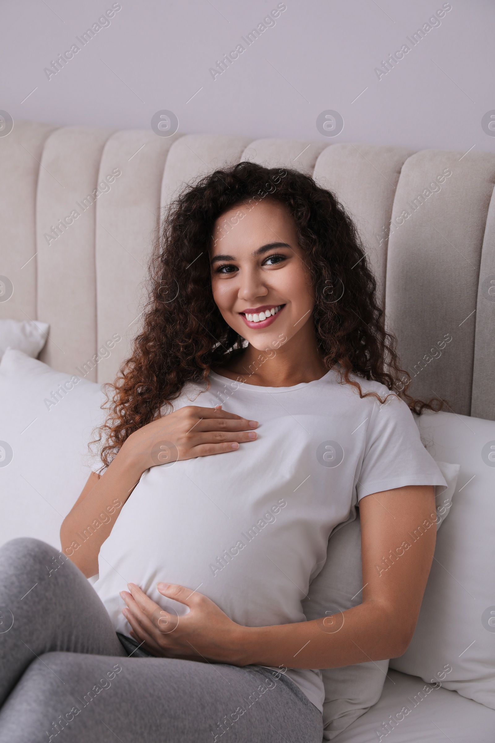 Photo of Pregnant young African-American woman sitting on bed at home