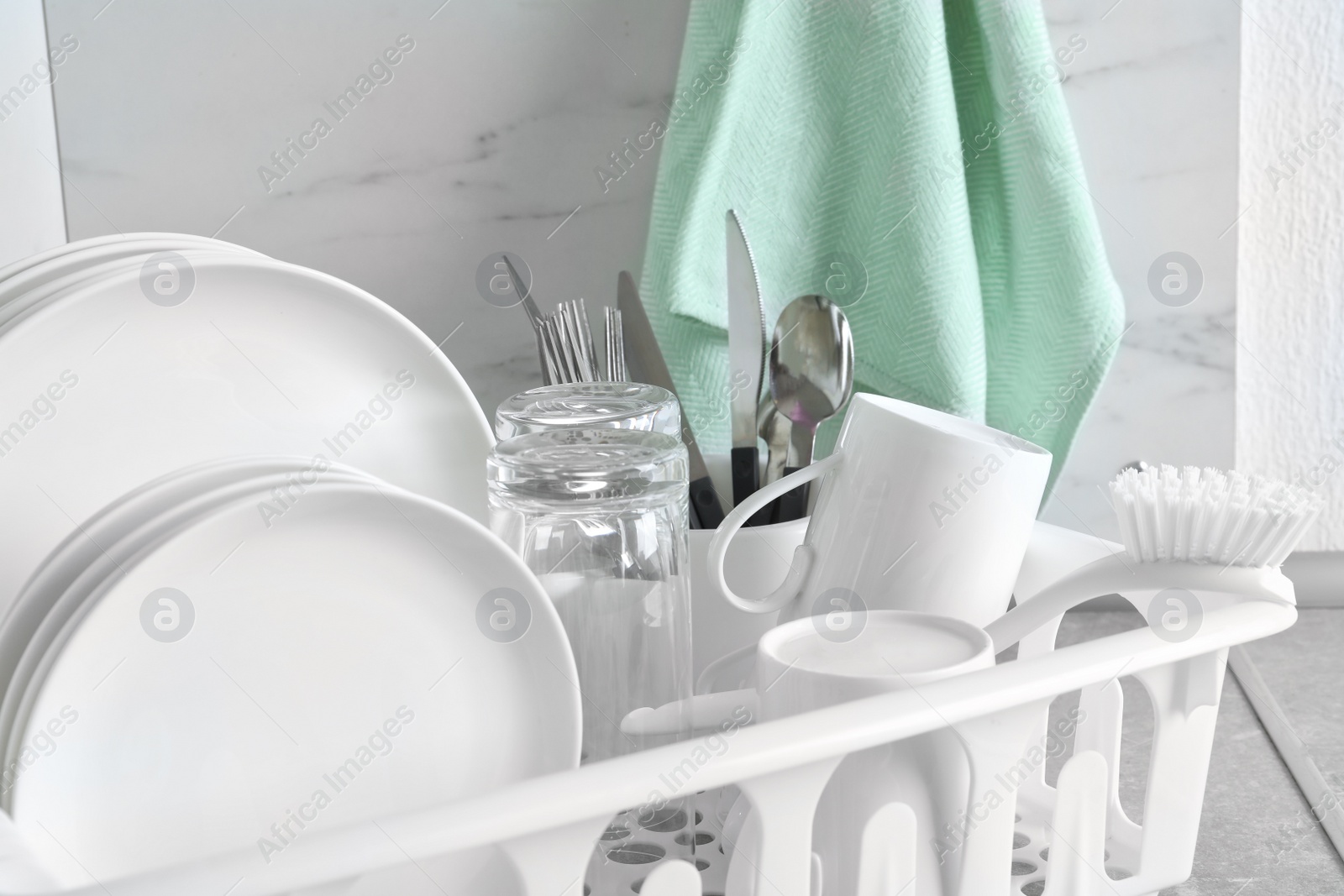 Photo of Drying rack with clean dishes and cutlery on table near light wall