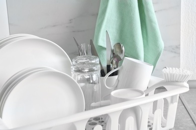 Photo of Drying rack with clean dishes and cutlery on table near light wall