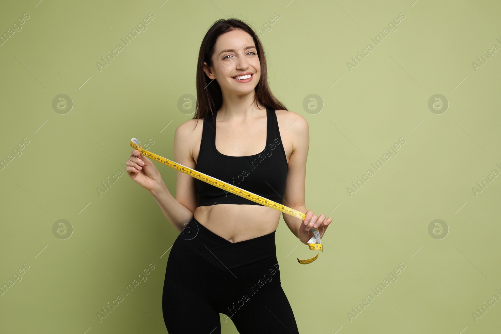 Photo of Happy young woman with measuring tape showing her slim body on green background