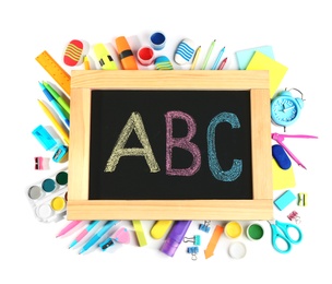 Photo of Small chalkboard with letters ABC and different school stationery on white background, top view