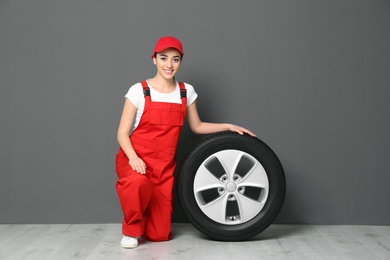 Photo of Female mechanic in uniform with car tire on grey wall background