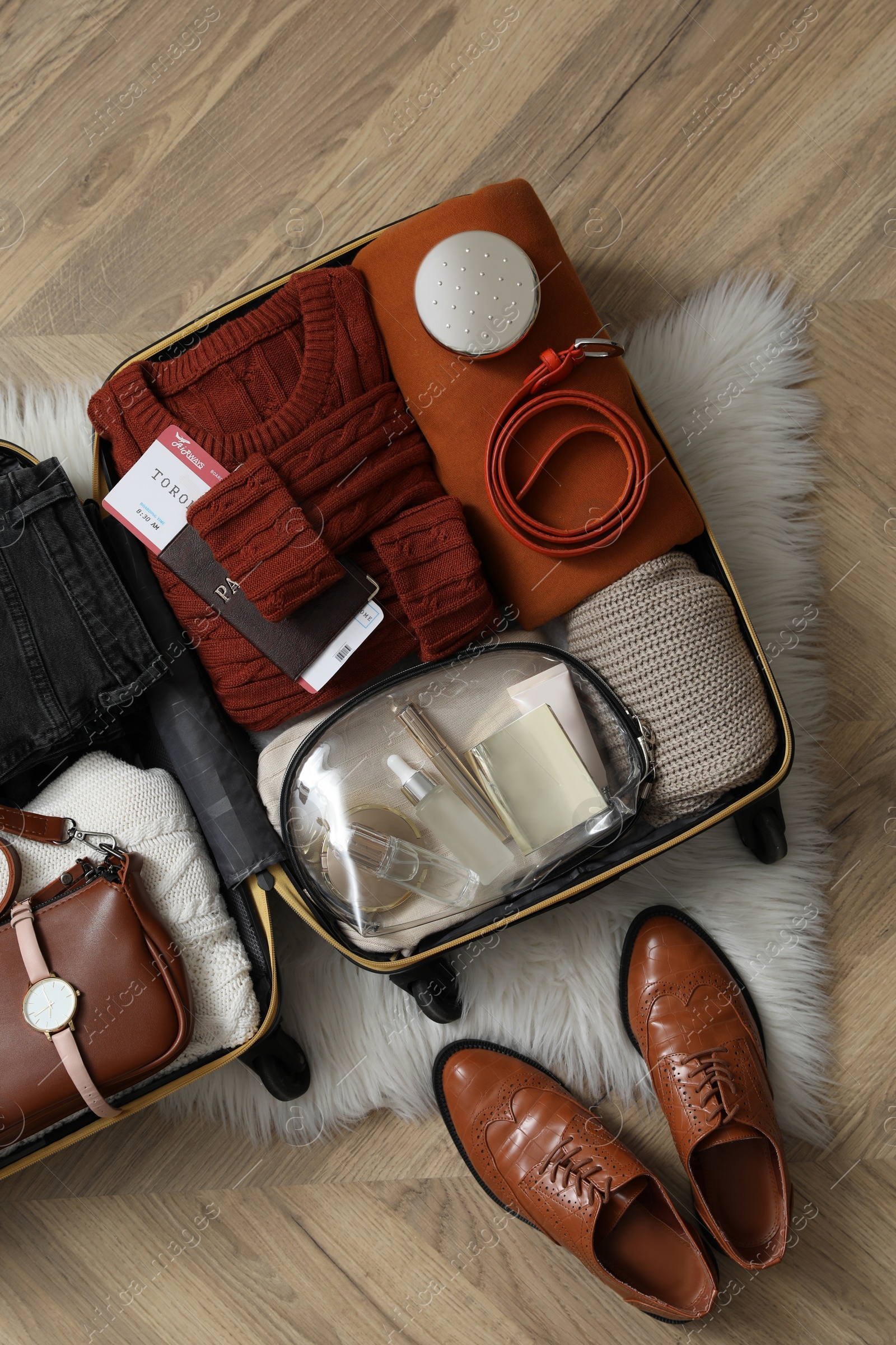 Photo of Open suitcase with folded clothes, accessories and shoes on floor, flat lay