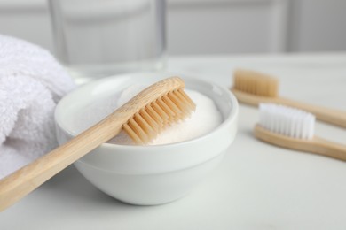 Photo of Bamboo toothbrushes, bowl of baking soda and towel on white table, closeup