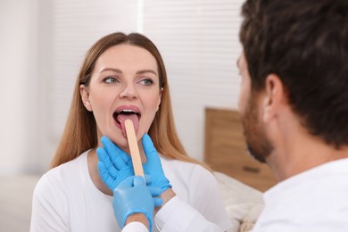 Photo of Doctor examining woman`s oral cavity with tongue depressor indoors