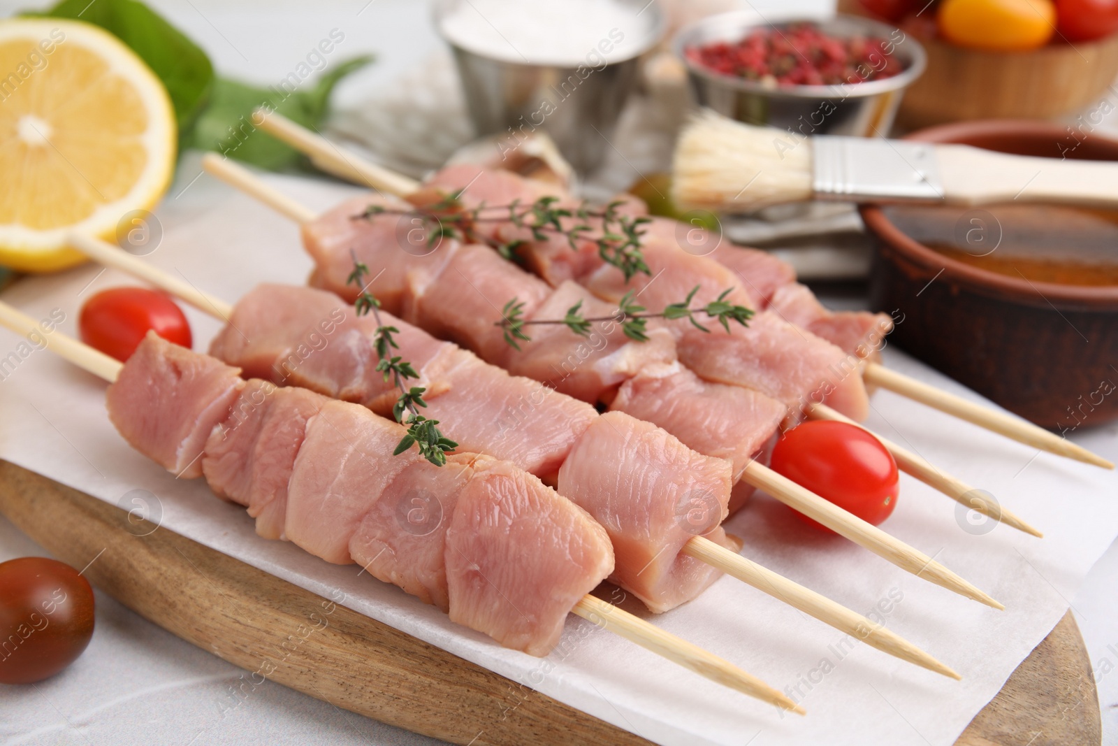 Photo of Skewers with cut raw meat, thyme and tomatoes on table, closeup