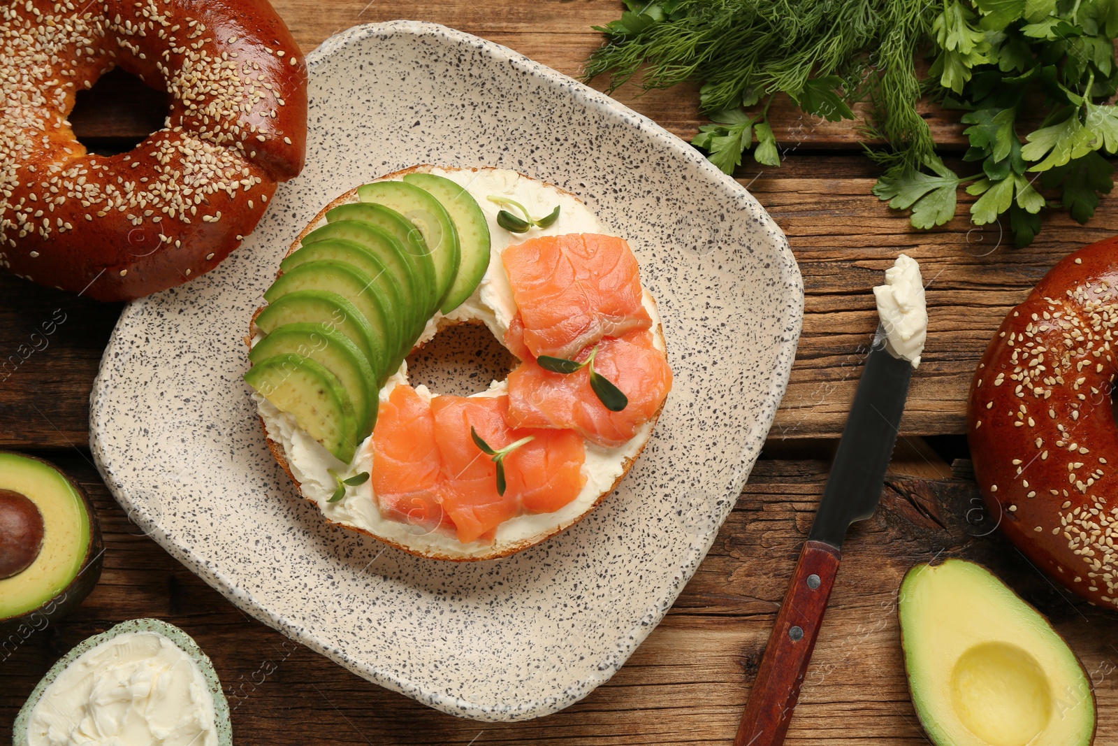 Photo of Delicious bagel with cream cheese, salmon and avocado on wooden table, flat lay