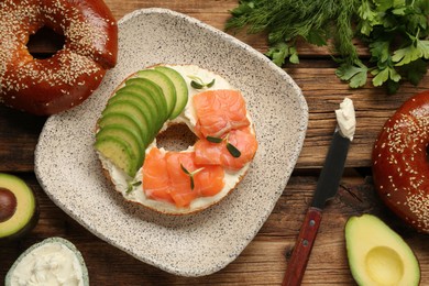Photo of Delicious bagel with cream cheese, salmon and avocado on wooden table, flat lay