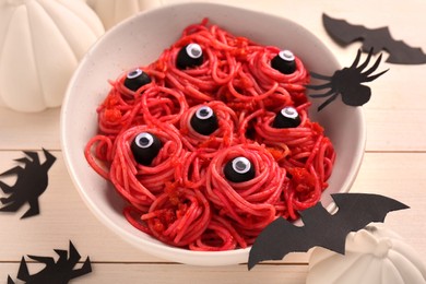 Photo of Red pasta with decorative eyes in bowl and Halloween decorations on white wooden table, closeup