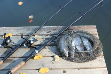 Photo of Fishing rods and fresh fish on wooden pier near pond