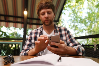 Photo of Handsome man using smartphone at table in outdoor cafe