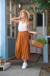 Photo of Young woman with basket of home plants on veranda
