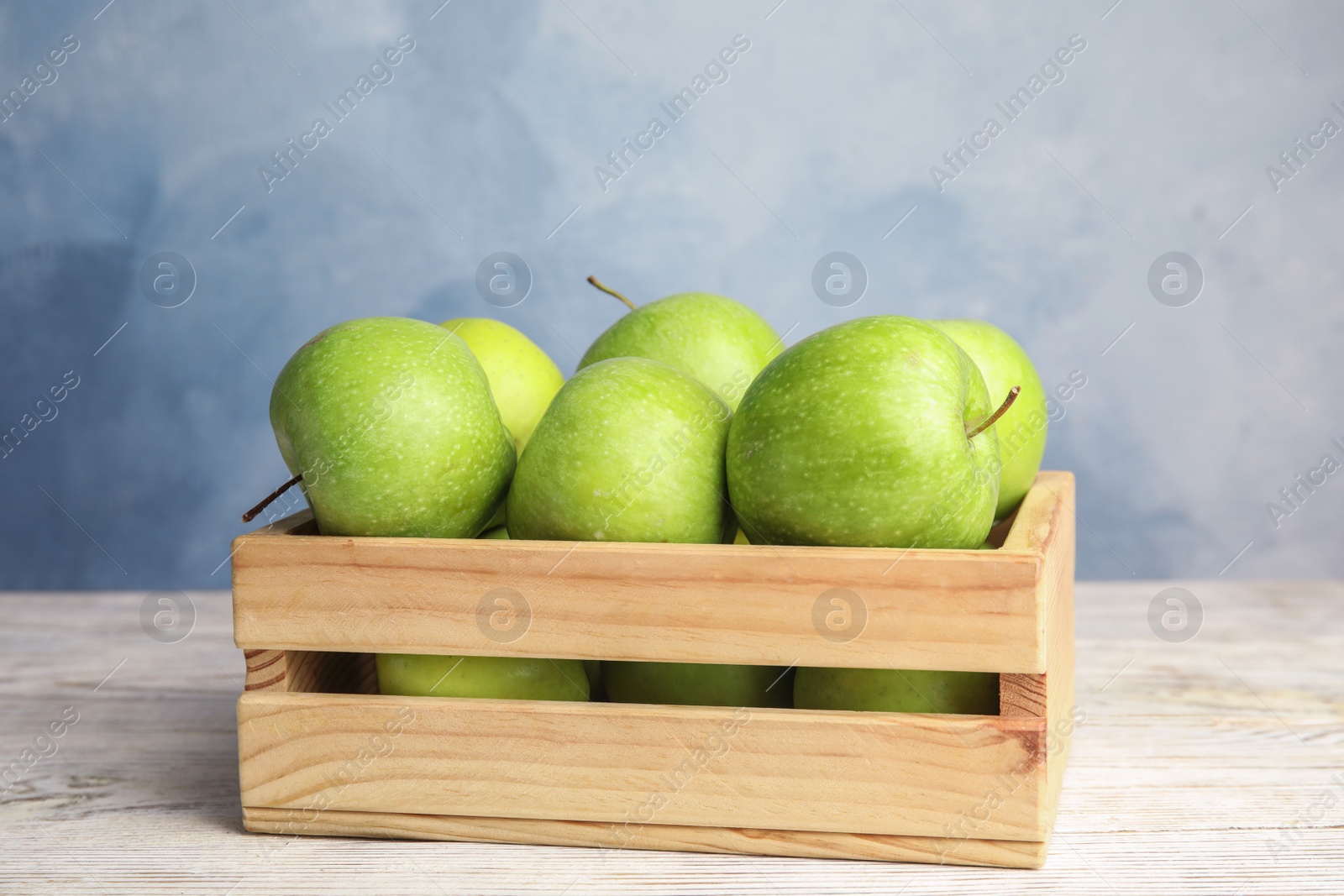 Photo of Wooden crate of fresh ripe green apples on white table against blue background, space for text