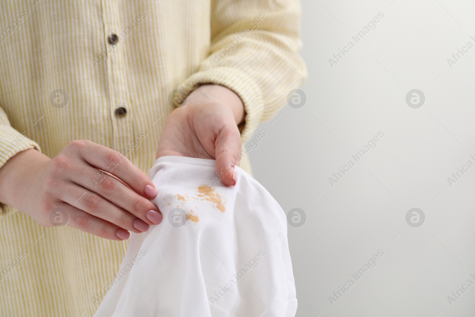 Photo of Woman holding shirt with stain against light background, closeup. Space for text