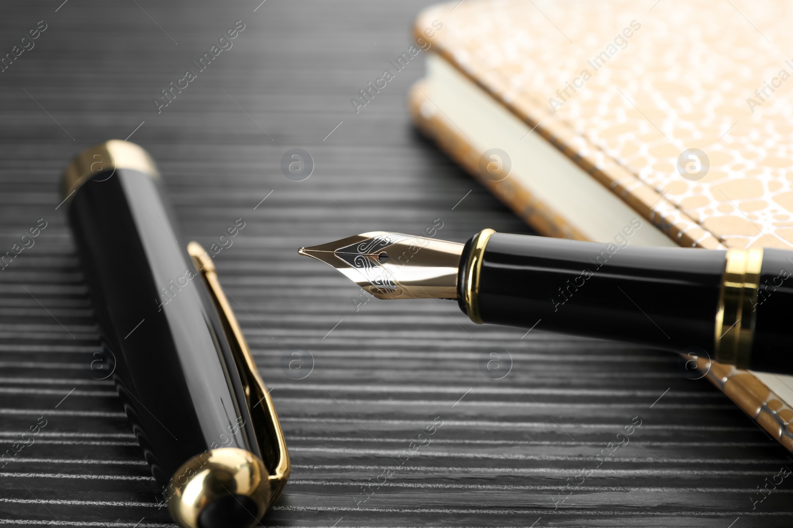 Photo of Stylish fountain pen and notebook on black wooden table, closeup