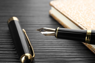 Photo of Stylish fountain pen and notebook on black wooden table, closeup