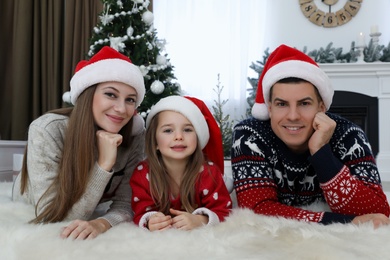 Happy family in Santa hats near Christmas tree at home