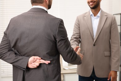 Photo of Employee crossing fingers behind his back while shaking hands with boss in office, closeup