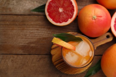 Photo of Tasty grapefruit drink with ice in glass and fresh fruits on wooden table, flat lay. Space for text