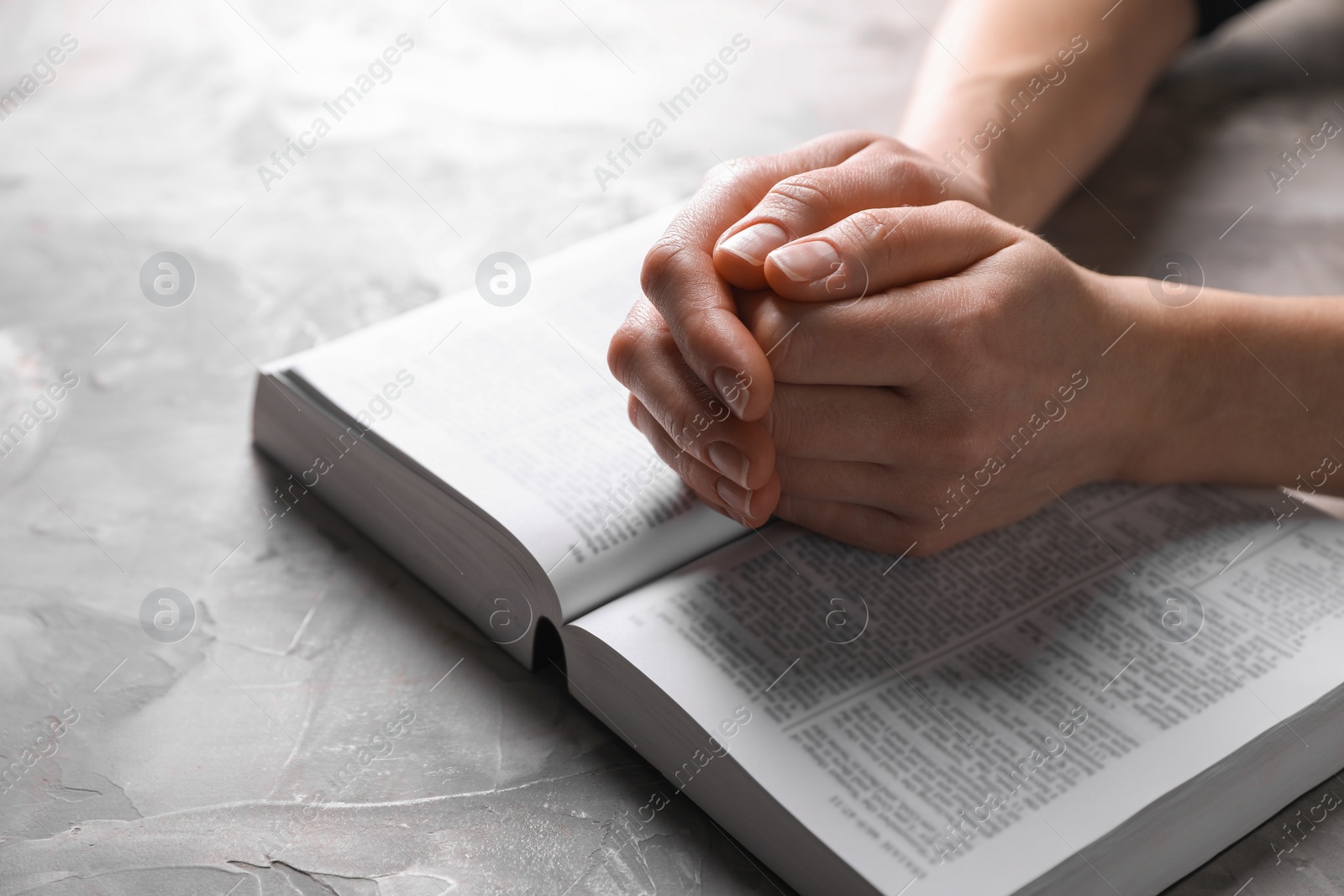 Photo of Religion. Christian woman praying over Bible at gray textured table, closeup