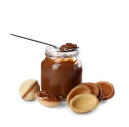 Jar with boiled condensed milk, spoon, cooked dough and walnut shaped cookies on white background