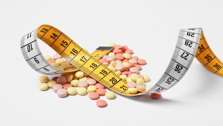 Photo of Weight loss pills and measuring tape on white background
