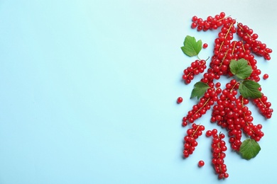 Photo of Delicious red currants and leaves on light blue background, flat lay. Space for text