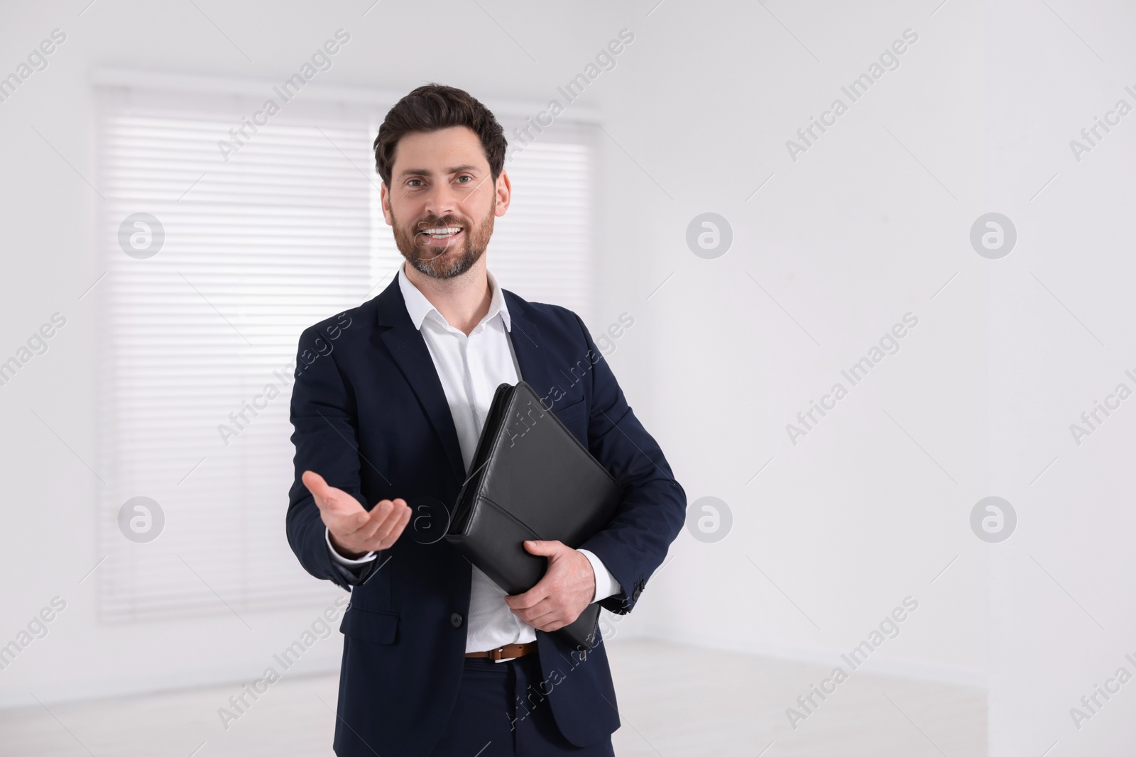 Photo of Happy real estate agent with leather portfolio indoors. Space for text