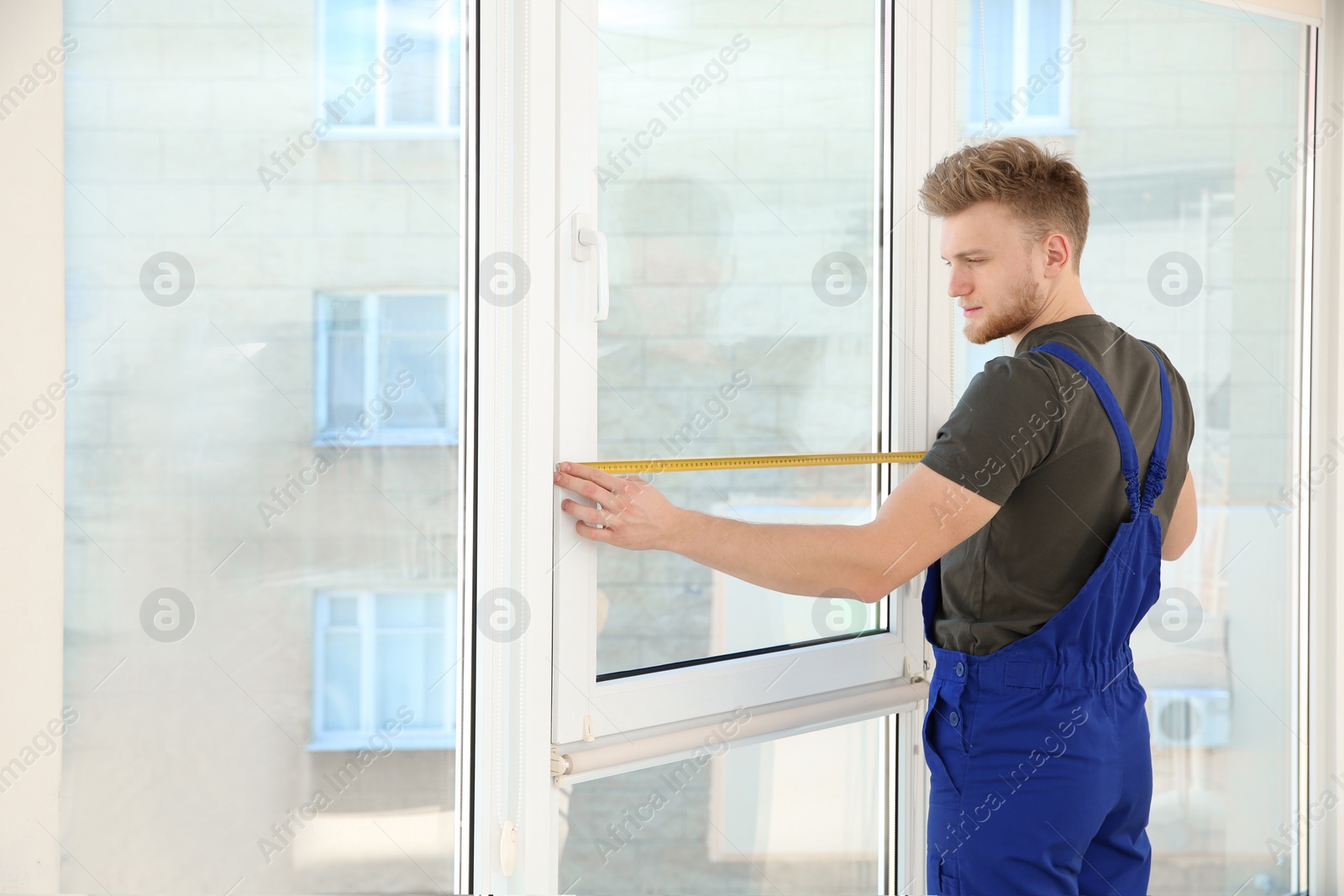 Photo of Service man measuring window for installation indoors. Space for text