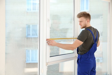 Service man measuring window for installation indoors. Space for text