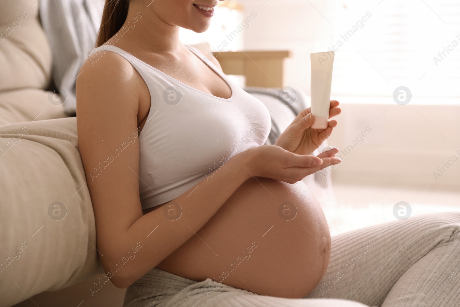 Photo of Young pregnant woman with cosmetic product at home, closeup
