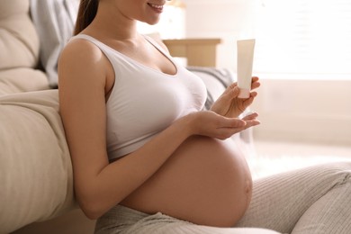 Photo of Young pregnant woman with cosmetic product at home, closeup